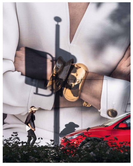 Cropped image of a billboard showing a woman with folded arms and gold bangles. A woman walks in front of the billboard towards a red car parked on the street