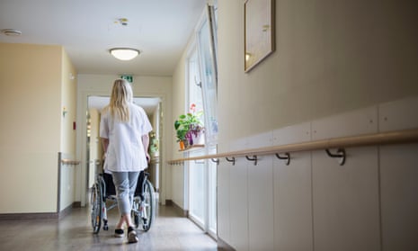 Rear view of nurse pushing wheelchair in hospital corridor
