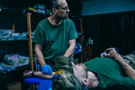 A medic is seen treating a soldier’s arm as he lies down on a bed 
