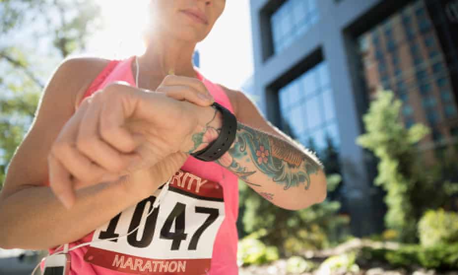 Tattooed female marathon runner checking smart watch in urban park