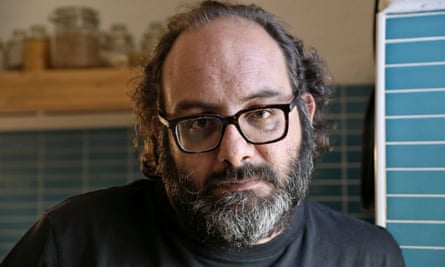 Fadi Kattan, with a dark beard and glasses, standing in a kitchen with blue tiles.