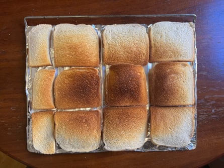 Top view of a baking tray lined with slices of white bread, in varying degrees of golden-brown toastiness.
