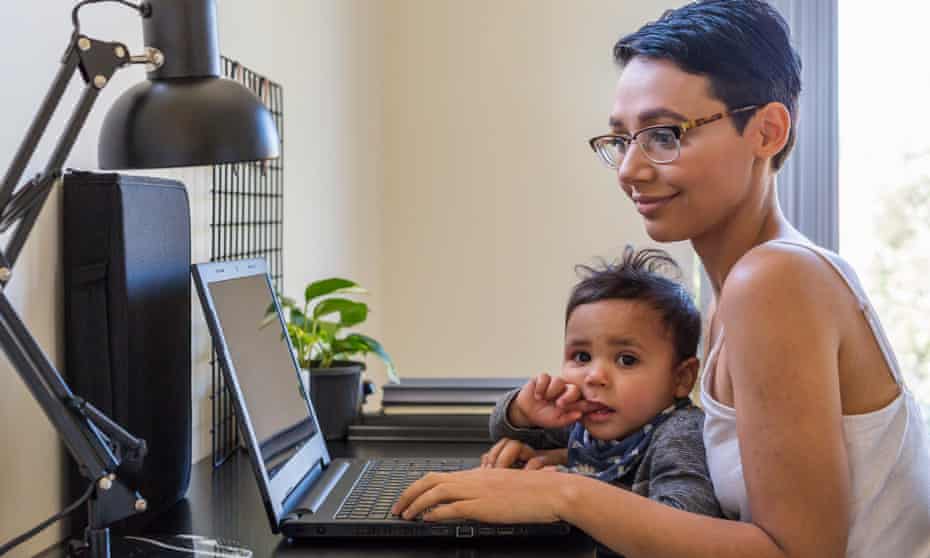 Young woman typing on a computer in a home office with her son on her lap