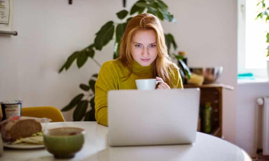 Woman drinking coffee and using laptop at home.