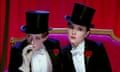Keely Hawes, left, and Rachael Stirling wearing top hats and suits while sitting on a velvet sofa