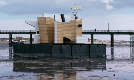 Flood House, a floating weather station, at low tide in front of a pier
