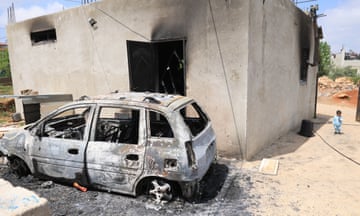 A burnt-out vehicle and smoke-damaged house in the West Bank village of Qusra, near Nablus, 14 April 2024