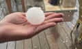 A hand holding a golfball-sized hailstone