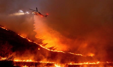 A helicopter drops water on a raging wildfire