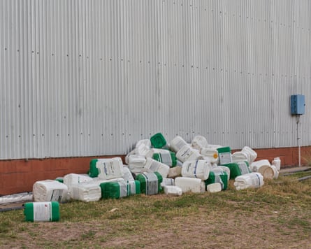 several empty containers of herbicides stacked in grass outside building