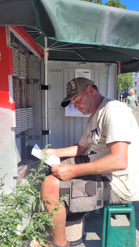Sven, 58, rewires a telecommunications box on a street in Berlin amid harsh sunlight.