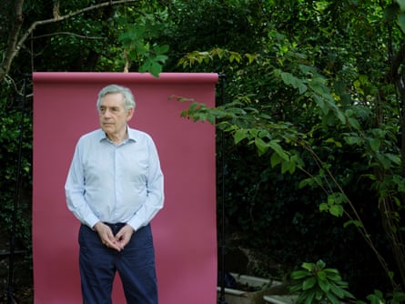 British politician Gordon Brown in pale shirt against burgundy background, with trees behind that