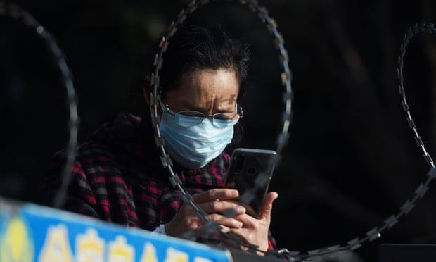 A woman uses her mobile phone behind barbed wire at an entrance of a residential compound in Wuhan
