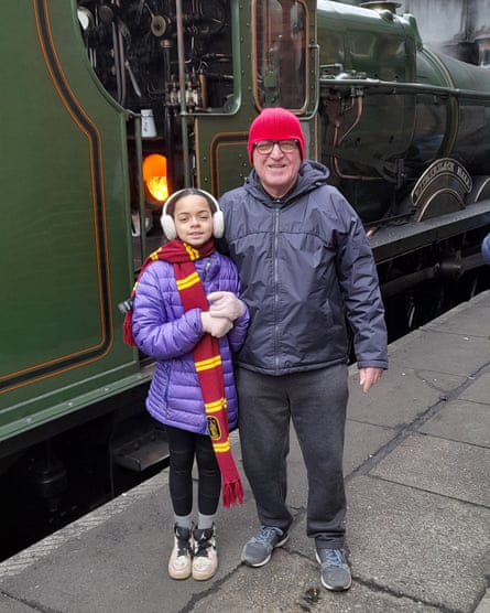 John Perry and his granddaughter Eva standing on a platform beside a green train.