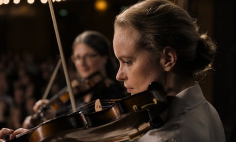 A woman plays the violin side on, with another looking on in the background
