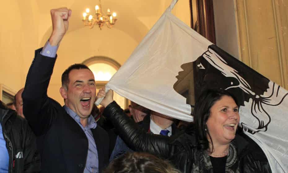 Gilles Simeoni (left), the mayor of Bastia and leader of the nationalists, celebrates victory in the French regional elections next to a Corsican flag.