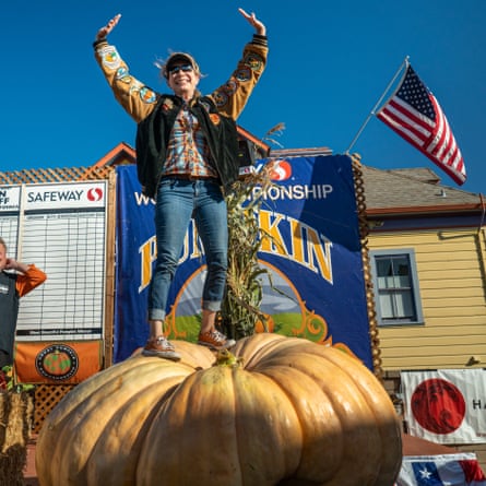 person with arms raised stands on giant pumpkin