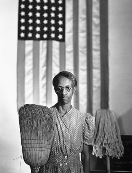 Blak and white image of a cleaner with a mop and broom standing in front of an American flag