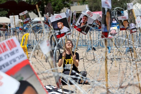 A woman holds placards with pictures of Israeli hostages Evyatar David and Rom Braslavski, held as hostages in Gaza, as she sits amid security wire in Tel Aviv