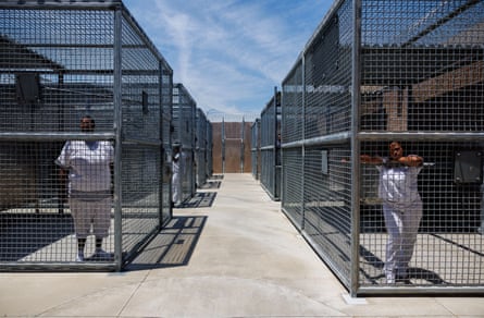 Two women stand in separate cages in a prison yard