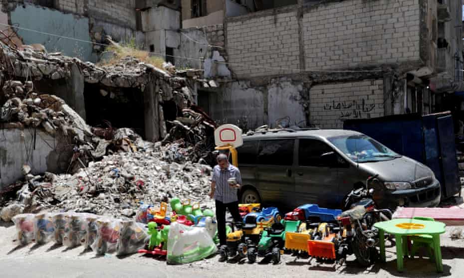 A street vendor sells toys next to rubble of damaged buildings in the city of Idlib.