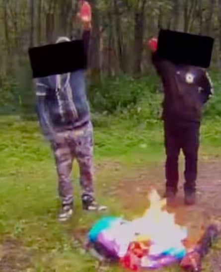 Two men in a forest, something on fire in front of them, both doing Nazi salutes and with black shapes across their faces to disguise their identity