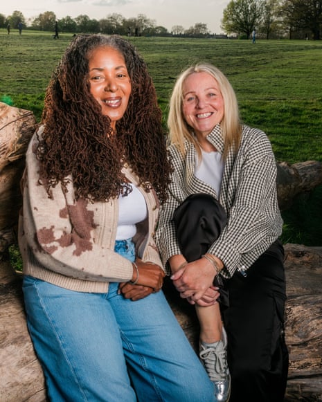 Two female friends sitting side by side on a log in a park