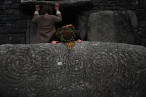 Os foliões tocam a pedra da entrada esculpida pelos célticos na tumba da idade da pedra de 5.000 anos de Newgrange, no condado de Meath, Irlanda.  A entrada dentro da câmara está fechada pelo segundo ano por causa da pandemia de Covid.