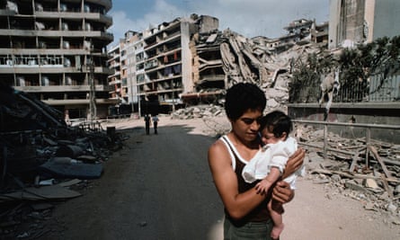 A father carries a young child near destroyed buildings