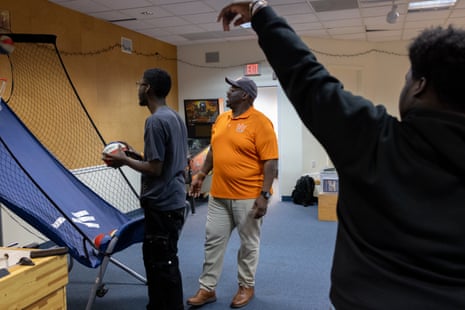 A man plays a basketball arcade game with two teens