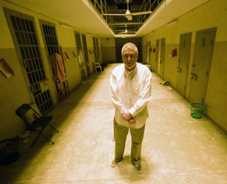 A man in a white shirt and beige trousers with short grey hair in a prison corridor