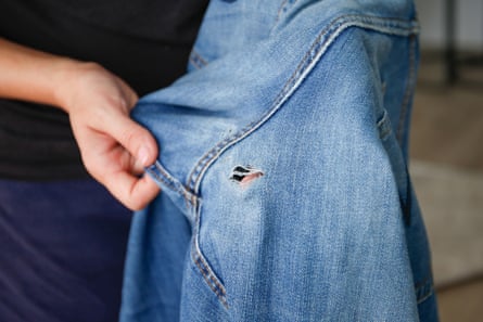 A woman holds up a pair of jeans with a hole