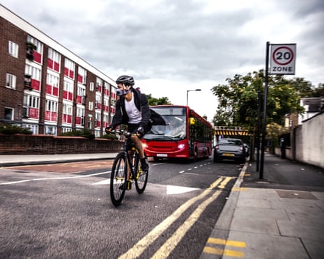 A cyclist rides through London while wearing a helmet and pollution mask