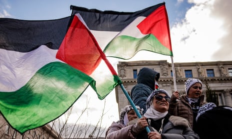 Women wearing keffiyehs waving red, black, white and green Palestinian flags.