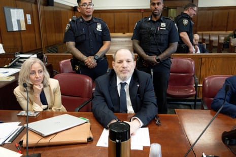 a man sits in court flanked by armed guards