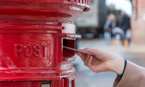 A woman placing a letter in a Royal Mail post box