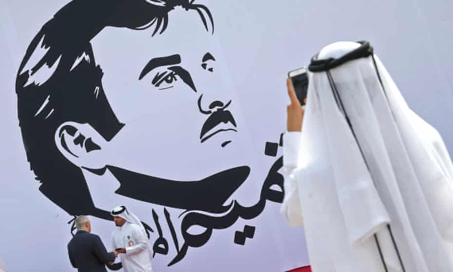 An observer takes a photograph of an image of Qatar’s emir, Tamim bin Hamad al-Thani, in Doha