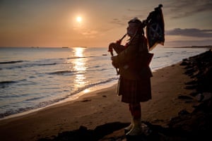 A lone piper in uniform plays on a beach at sunrise