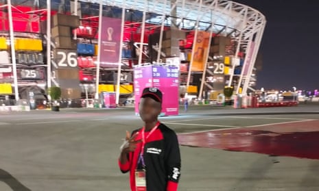 A black security guard in a uniform standing outside a stadium made from old shipping containers