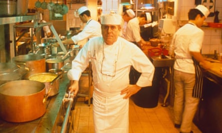Chef Albert Roux standing in the kitchen of Le Gavroche wearing chef whites next to a stove with pots.  