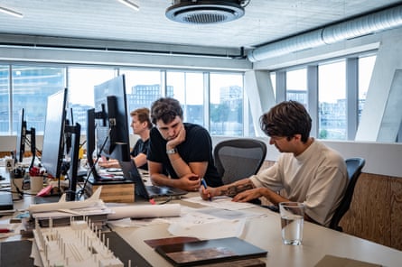 Three men in a modern, brightly lit office working on computers and drawings