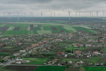 Wind turbines on grey horizon with green fields and village in foreground