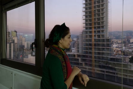 A young Arab woman in a tower block looks out of a window at a city’s skyline