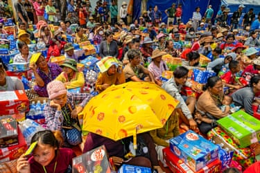 Rows and rows of people sitting on the ground next to donations in colourful boxes