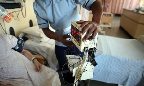 A nurse checking a monitor next to a patient in a hospital gown