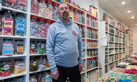 Steve Barnes standing in front of shelves of sweet jars that run the length of the wall, with more sweets on the table in front of him