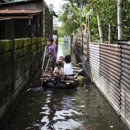 Children use a raft to cross a flooded alley in Calumpit, Bulacan, after Typhoon Mangkhut