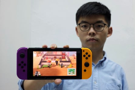 Pro-democracy activist Joshua Wong poses with a Nintendo Switch where depictions of anti-government protesters and signs saying “Free Hong Kong” are seen in the game Animal Crossing.