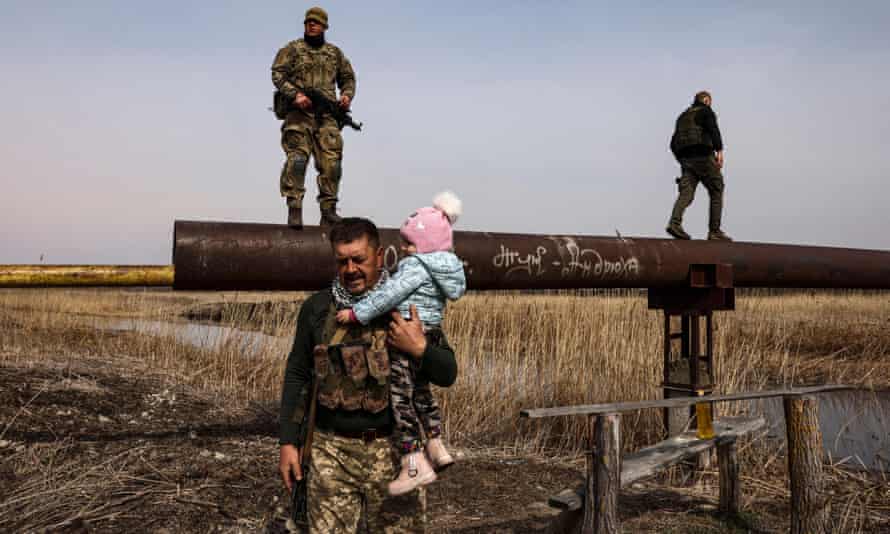 A Ukrainian serviceman carries the baby of a displaced family to help to cross a river, on the outskirts of Kyiv.