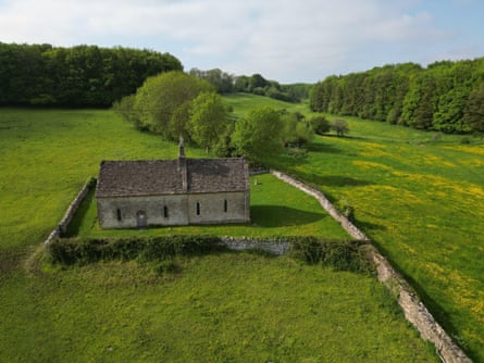 An aerial view of a very old church set in fields and near woods in England.